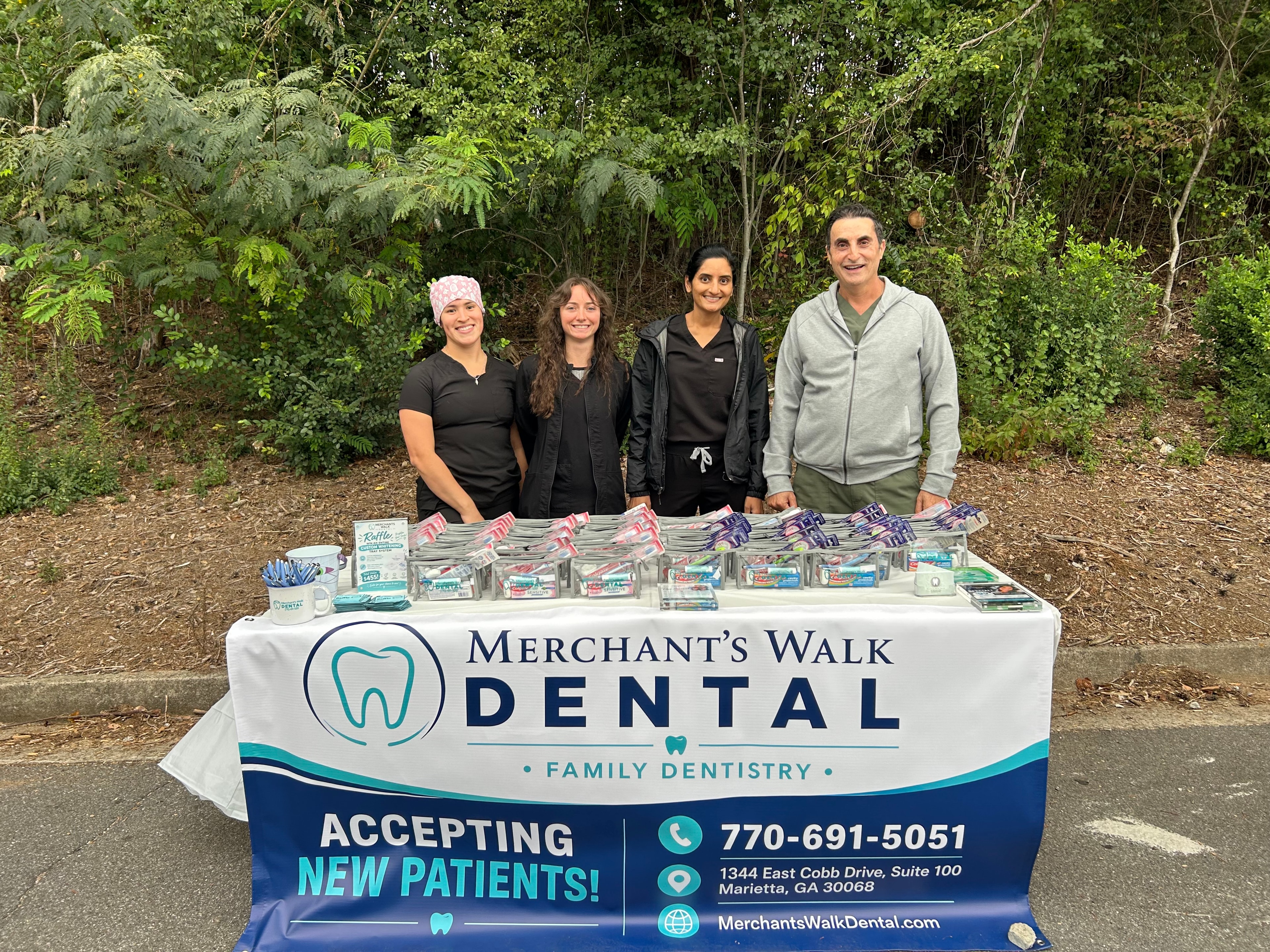 Claudia, Briana, Dr. Patel, and Dr. Bishara standing behind the Merchants Walk Dental sponsor table at the Timber Ridge Fall Festival